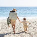 Woman with backpack beach chair walking with  child on a sandy beach with ocean in the background