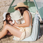 mum sitting on a beach chair with a baby and toddler with a beach tent in the background