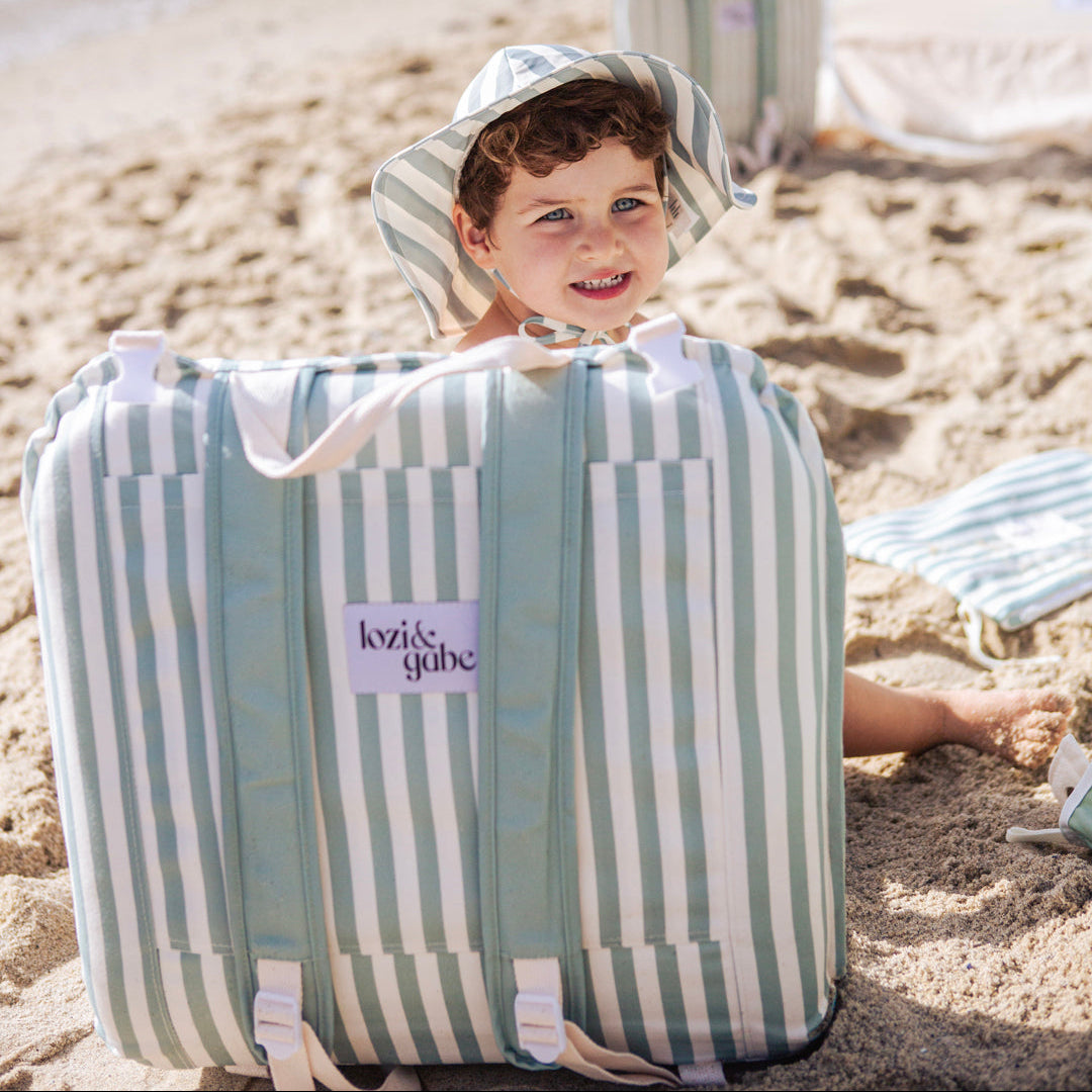 Child sitting on a striped beach chair on a sandy beach.