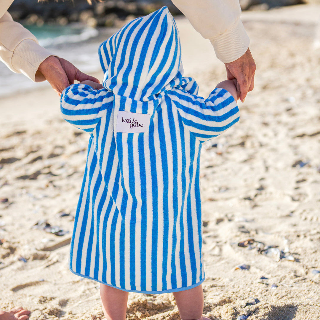 Child wearing a blue and white striped beah poncho on a sandy beach