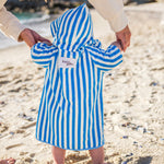 Child wearing a blue and white striped beah poncho on a sandy beach