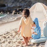 Two children on a beach  wearing striped ponchos with a tent in the background