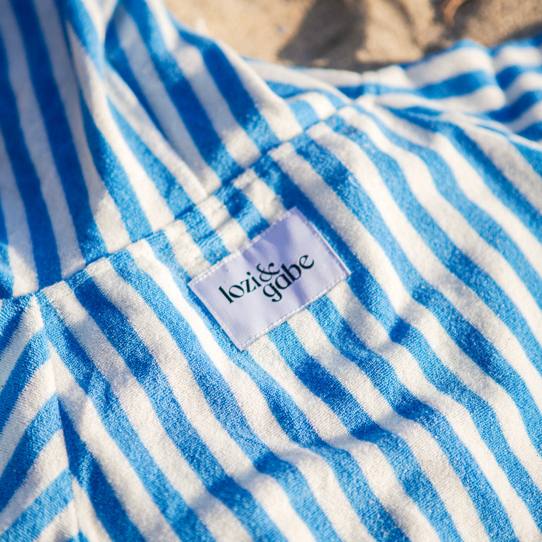Close-up of a blue and white striped beach poncho with a lozi and gabe label on the back